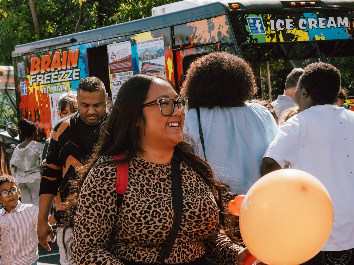A woman laughing in front of the ice cream truck, orange balloon in hand