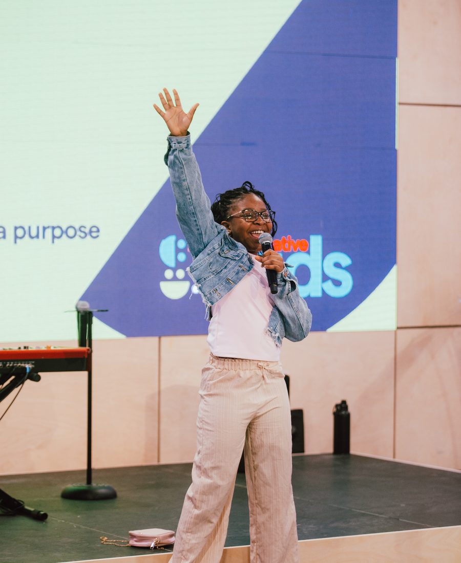 A girl on the Creative Kids stage with a microphone, one hand in the air