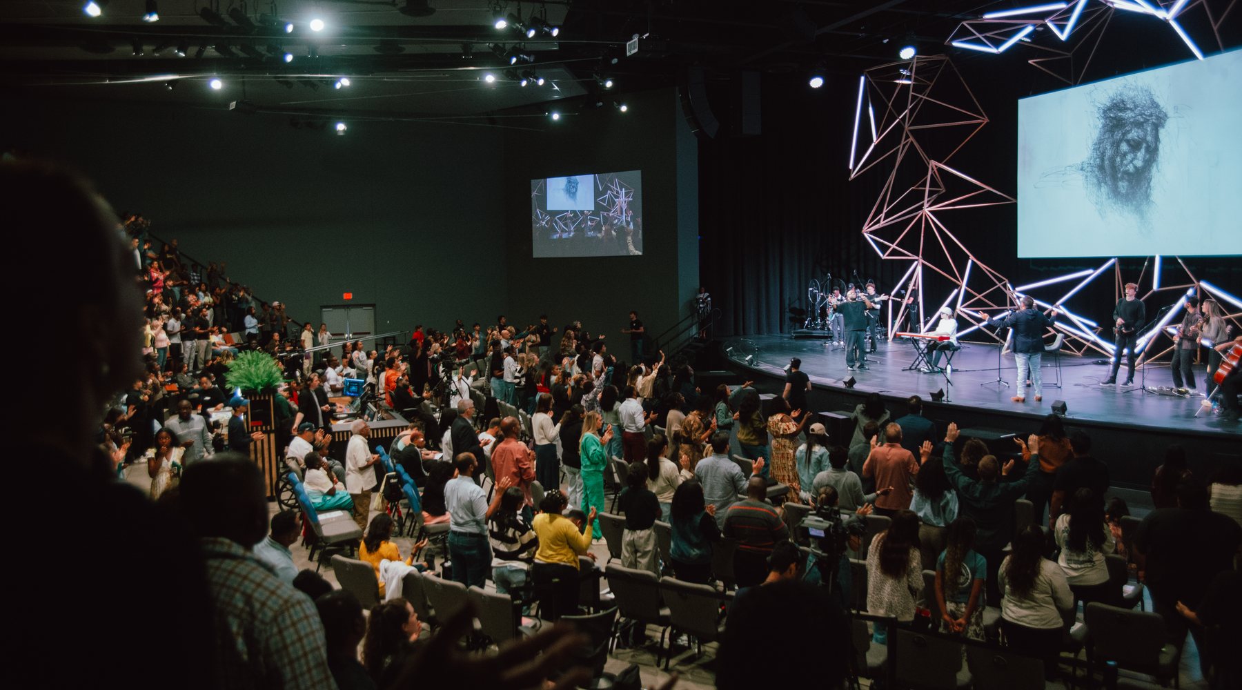 The room at Creative Church during worship, hands raised, the band on stage