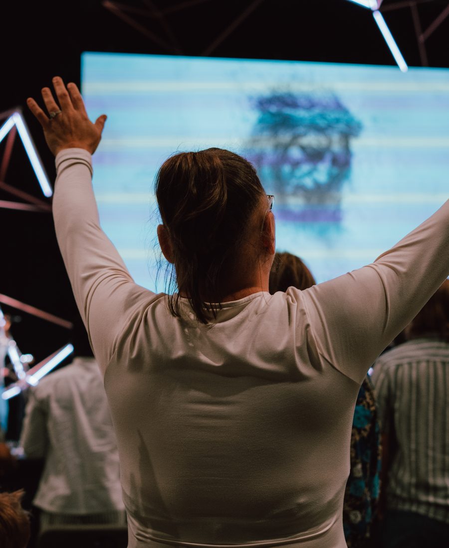 A woman with both hands raised during worship, seen from behind